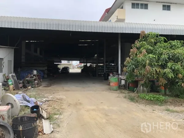 คลังสินค้า ให้เช่าในSai Noi, Nonthaburi - มุมทางเข้าหลังโกดัง ทางดินกว้าง มีหลังคาคลุม ต้นไม้และถังเก็บของ