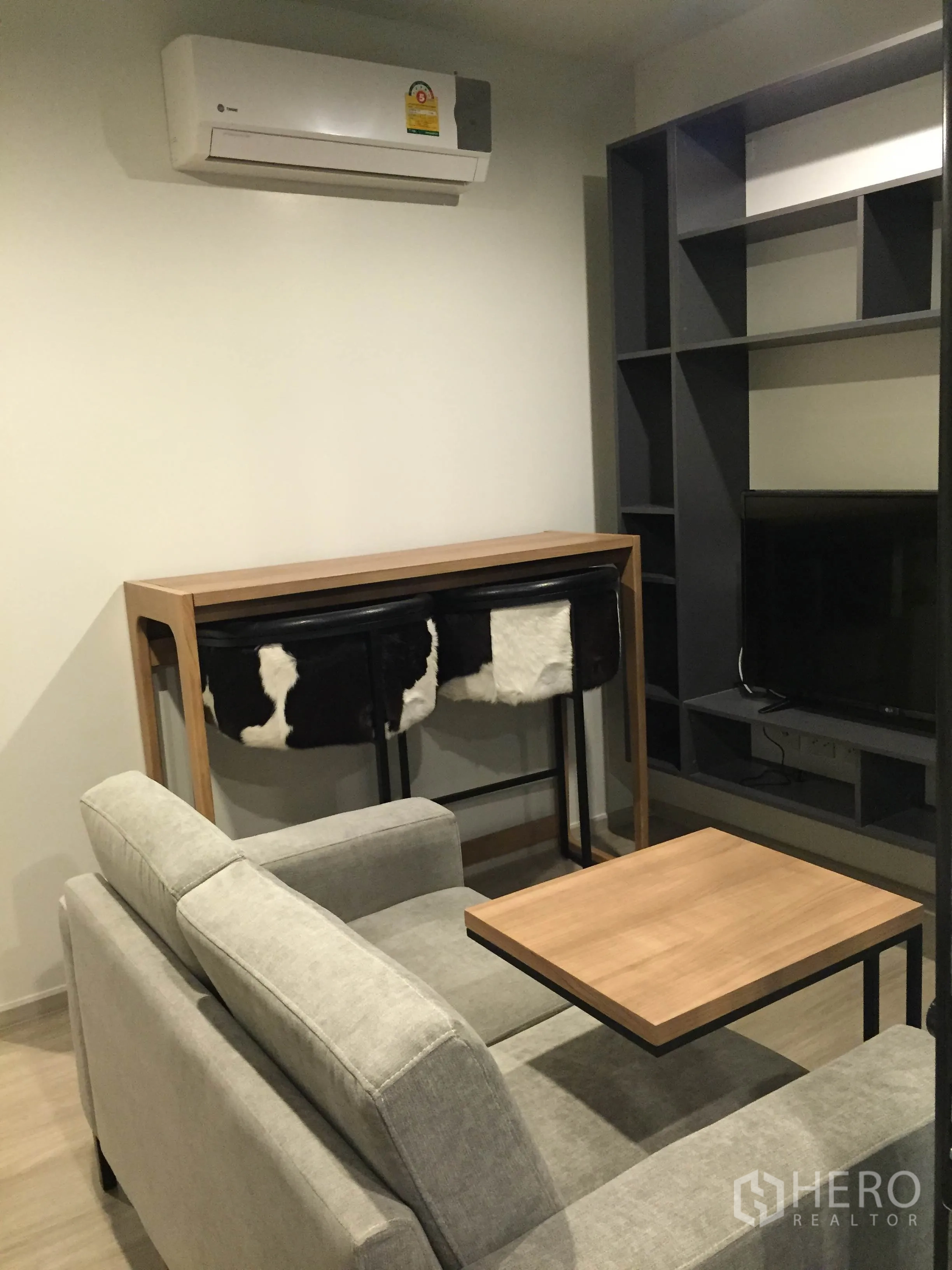 Condominium for rent in Pathum Wan, Bangkok - Cozy living area with grey sofa, wall-mounted air conditioner and wooden coffee table.
