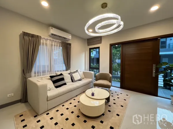 บ้าน ให้เช่าในBang Phli, Samut Prakan - ห้องนั่งเล่นสว่างโทนอบอุ่น โซฟาตัวใหญ่ โคมไฟวงแหวน และประตูไม้บานใหญ่