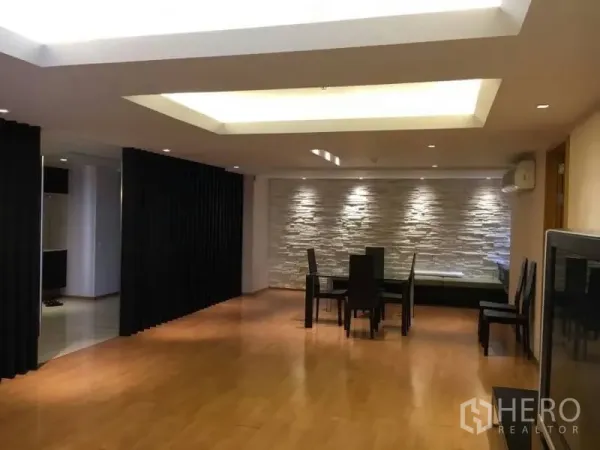 Condominium for rent in Watthana, Bangkok - Open-plan dining area with wood floors, cove ceiling lights, and a stone accent wall.