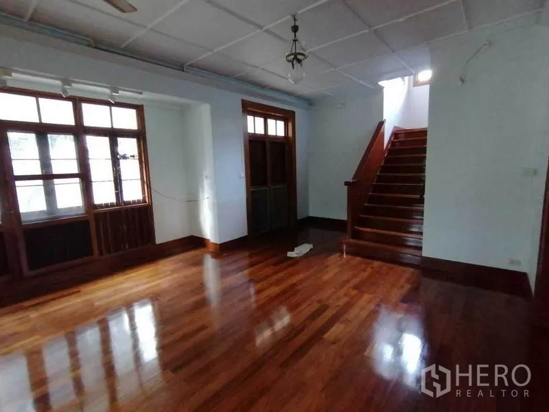 Detached House for rent in Pathum Wan, Bangkok - Living area with large windows and staircase to the upper level.