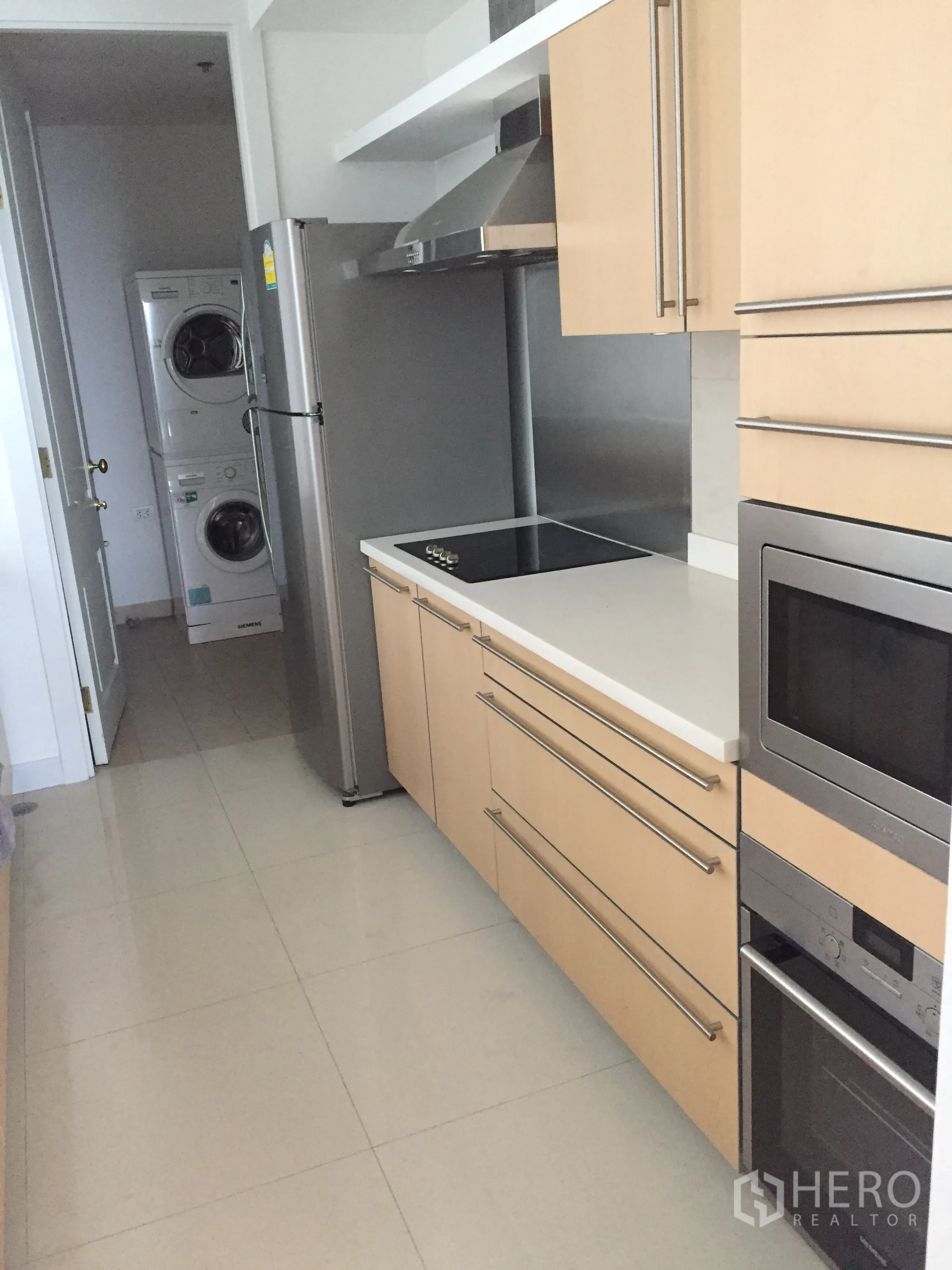 Condominium for rent in Pathum Wan, Bangkok - Modern galley kitchen with light wood cabinetry, built-in oven, cooktop and stacked washer–dryer.