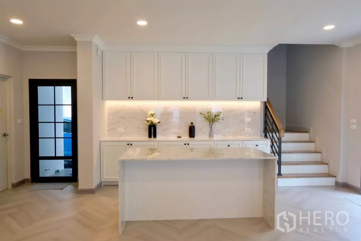 Detached House for sale in Bang Phli, Samut Prakan - Built-in white kitchen with marble backsplash, LED under-cabinet lighting and central island beside the stairs