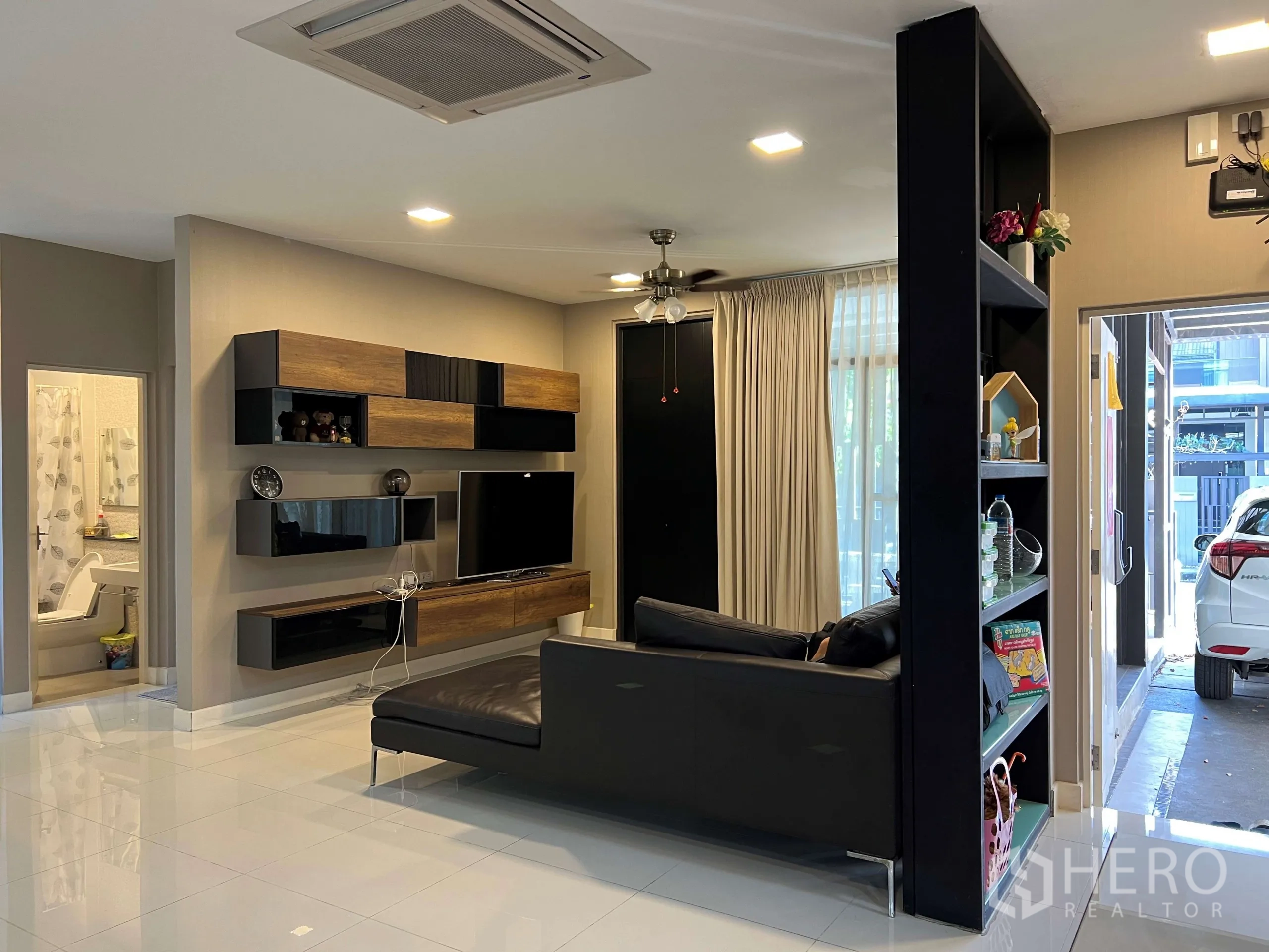 Detached House for rent in Prawet, Bangkok - Bright living room with wall-mounted TV unit, sofa, large windows and an adjacent bathroom.