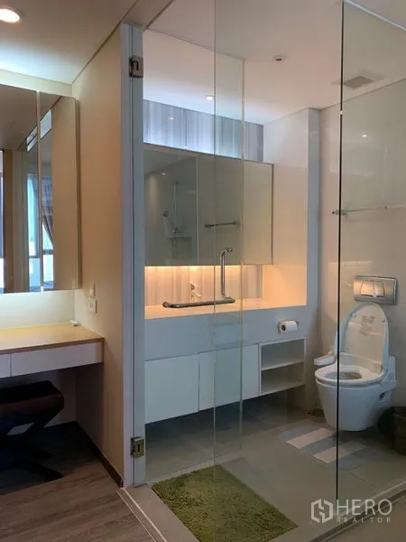 Condominium for rent in Watthana, Bangkok - Modern bathroom with glass partition, illuminated vanity, toilet and a dressing counter.