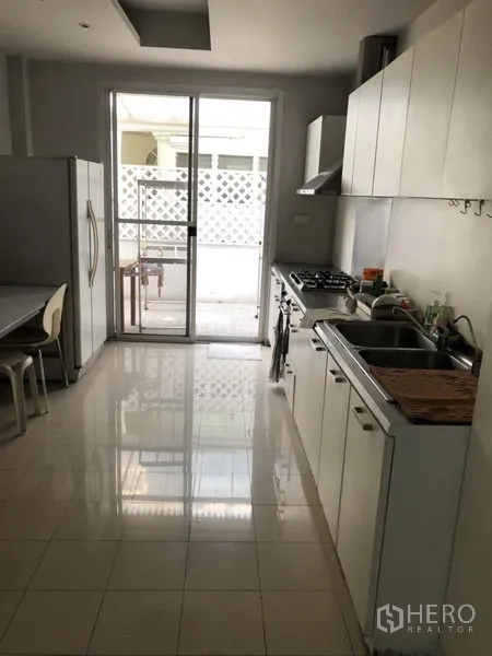 Detached House for rent in Chatuchak, Bangkok - Bright kitchen with white cabinets, gas cooktop, double sink and sliding door to terrace.