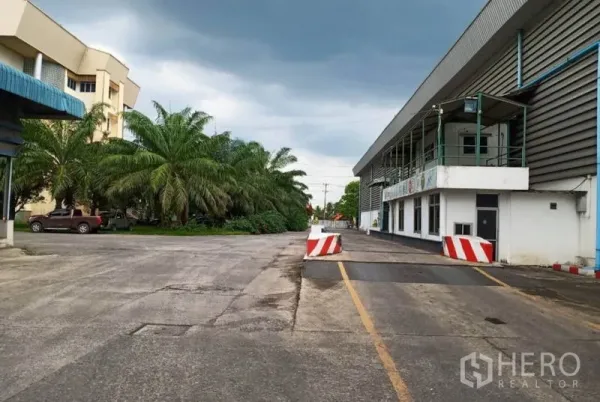 Factory for rent in Ban Phaeo, Samut Sakhon - Wide internal road with palm trees, office block and loading dock within a large factory complex.
