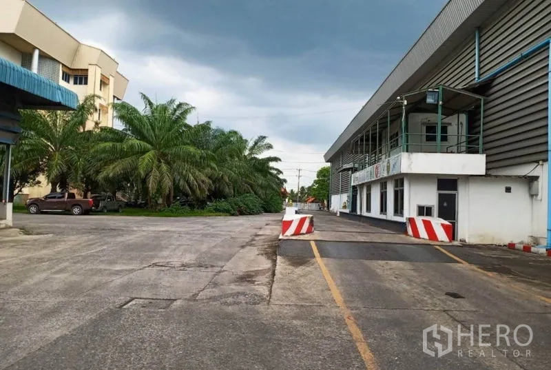 Factory for rent in Ban Phaeo, Samut Sakhon - Wide internal road with palm trees, office block and loading dock within a large factory complex.