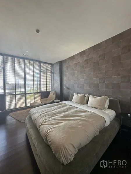 Condominium for rent or sale in Sathon, Bangkok - Spacious bedroom with textured wall, upholstered bed, and seating by the window.