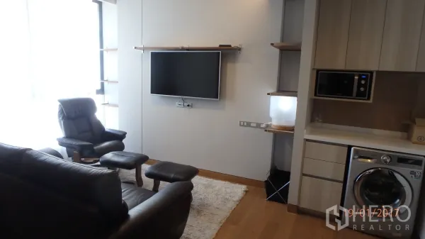 คอนโด ให้เช่าในKhlong Toei, Bangkok - ห้องนั่งเล่นสว่างเฟอร์นิเจอร์หนัง ทีวีติดผนัง หน้าต่างบานใหญ่ พื้นไม้ และแพนทรีพร้อมเครื่องซักผ้า