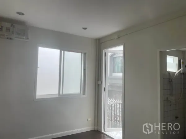 บ้าน ให้เช่าในHuai Khwang, Bangkok - ห้องภายในสว่าง มีหน้าต่างและประตูกระจกออกสู่ระเบียงเล็ก ติดกับห้องน้ำปูกระเบื้องพร้อมฝักบัว.