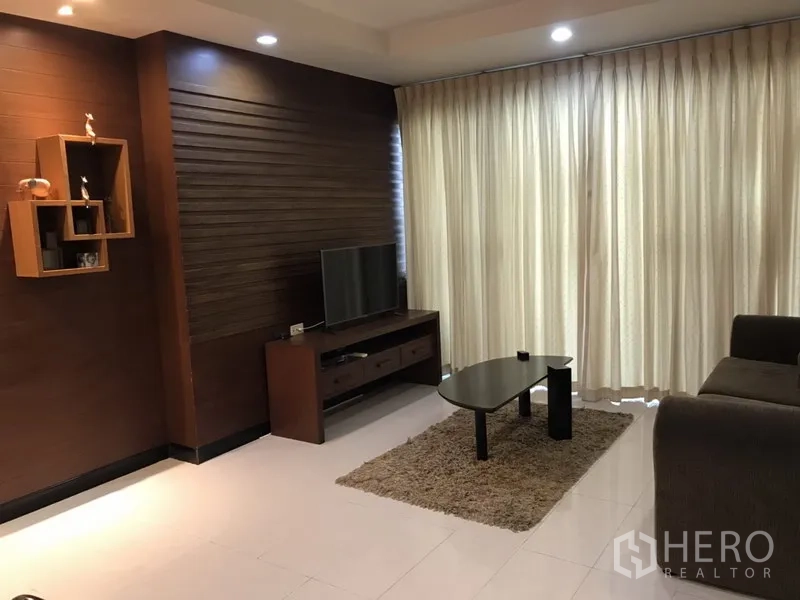 Condominium for rent in Watthana, Bangkok - Cozy living room with sofa, TV console, coffee table and floor‑to‑ceiling curtains.