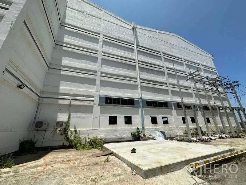 Factory for rent in Mueang Samut Prakan, Samut Prakan - Concrete service yard beside the factory wall with utility structures and platform.