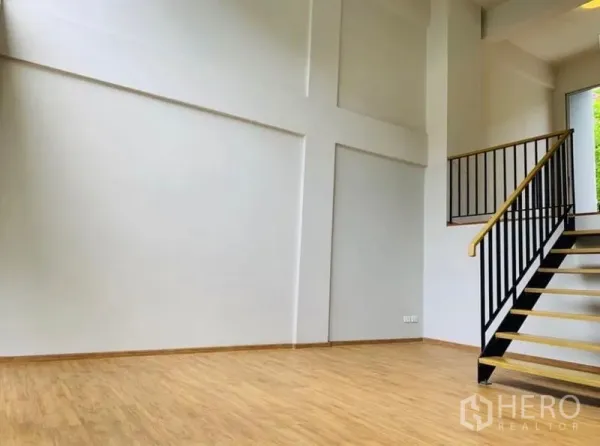 Home Office for rent - Spacious white-walled room with high ceiling and black metal stair railing on wood flooring.