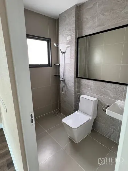 Detached House for rent or sale - Bathroom with beige tiles, shower, toilet and a wide mirror by the window.