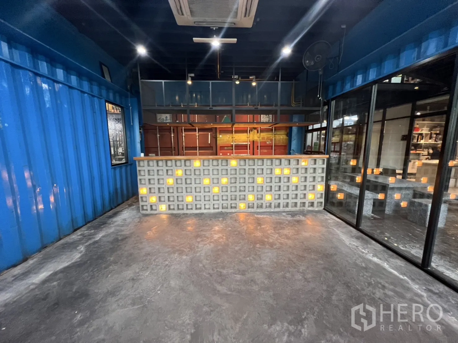 พื้นที่ขายปลีก ให้เช่า - ภาพด้านหน้าของเคาน์เตอร์บริการบล็อกแก้วเรืองแสงกับชั้นเหล็ก ในห้องสไตล์ตู้คอนเทนเนอร์