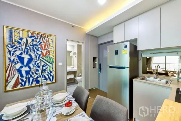 Condominium for rent in Phra Khanong, Bangkok - Dining corner beside kitchenette and stainless refrigerator, with a door leading to a bright bathroom.