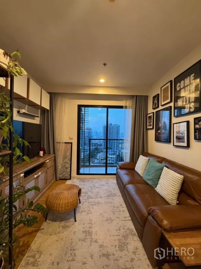 Condominium for rent in Watthana, Bangkok - Bright lounge with large rug, rattan ottoman and a balcony framing Bangkok skyline.