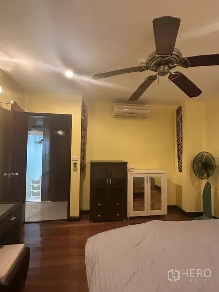 Condominium for sale in Watthana, Bangkok - Bedroom angle showing ceiling fan, air conditioner, freestanding cabinets and wood floors.
