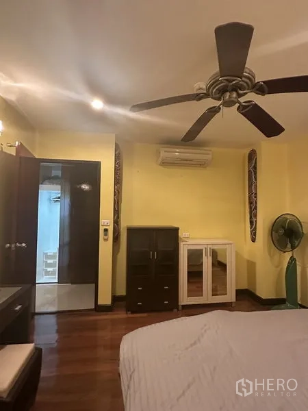 Condominium for sale in Watthana, Bangkok - Bedroom angle showing ceiling fan, air conditioner, freestanding cabinets and wood floors.