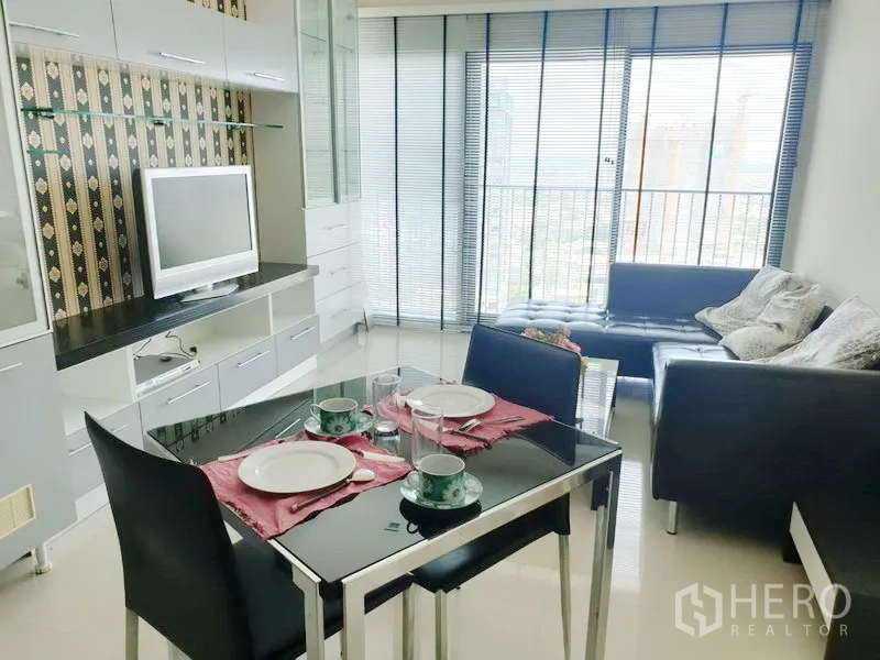 คอนโด ให้เช่าในKhlong Toei, Bangkok - ห้องนั่งเล่นและทานอาหารสว่าง พร้อมผนังบิลท์อิน โต๊ะกระจก โซฟาหนัง และระเบียงวิวเมืองพร้อมม่านปรับแสง