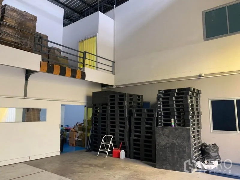 คลังสินค้า ให้เช่าในBang Kapi, Bangkok - โซนโหลดชั้นล่างพร้อมพาเลทพลาสติกกองตั้งและออฟฟิศบนชั้นลอยแบบปิด.