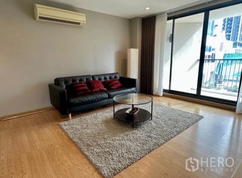 Condominium for rent in Watthana, Bangkok - Living area with black leather sofa, rug and sliding doors to the balcony.