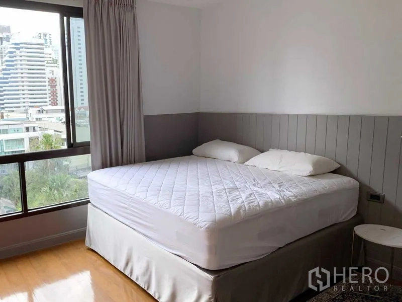 Condominium for sale in Watthana, Bangkok - Corner bedroom with large window, city view and gray wainscoting around a king bed.