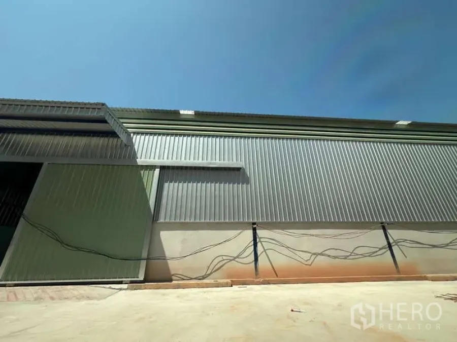 Warehouse for rent in Lat Krabang, Bangkok - Side view of the warehouse facade with large metal cladding and wide driveway suitable for truck access.