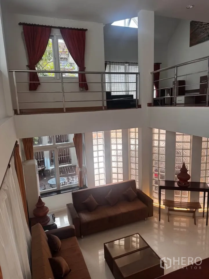 ทาวน์เฮาส์ for rent in Huai Khwang, Bangkok - มุมมองจากชั้นลอยลงสู่ห้องนั่งเล่นเพดานสูงพร้อมโซฟาและผนังกระจกบล็อก.