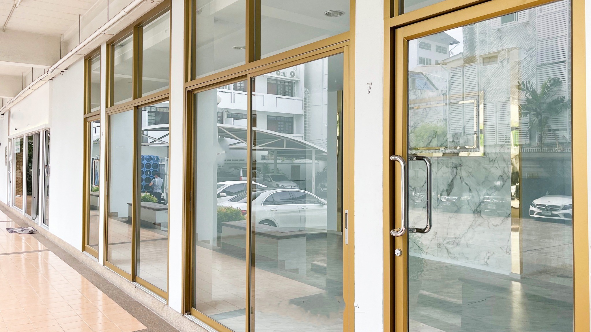 零售空间 出租在Watthana, Bangkok - 街向玻璃门面，金色框滑动门，连廊下门前，外侧可见停车区。