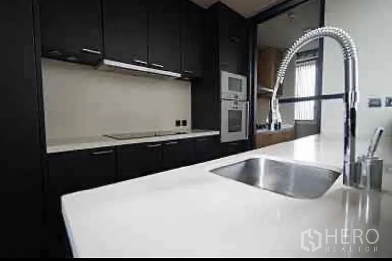 公寓 出租在Sathon, Bangkok - 厨房操作台配不锈钢水槽与弹簧龙头，对面为深色橱柜与嵌入电器。