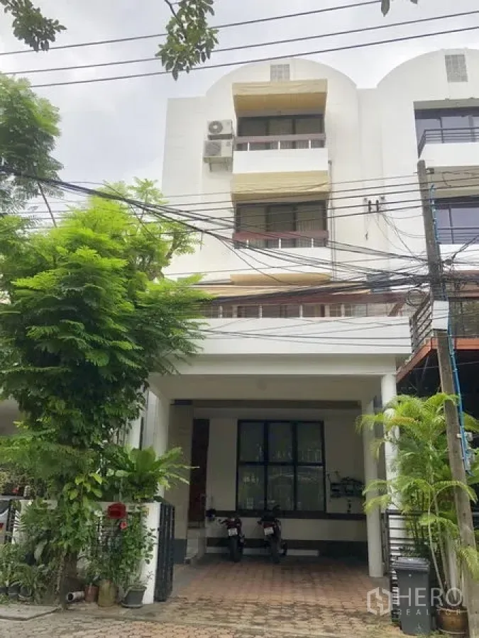 ทาวน์เฮาส์ ให้เช่าหรือขายในBangkok - ด้านหน้าทาวน์เฮ้าส์สีขาว 4 ชั้น มีที่จอดรถในร่มและต้นไม้ริมทางเดิน