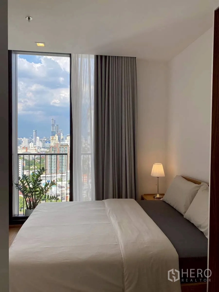 Condominium for rent in Watthana, Bangkok - Bright bedroom with double bed, lamp, and floor-to-ceiling window overlooking the city.
