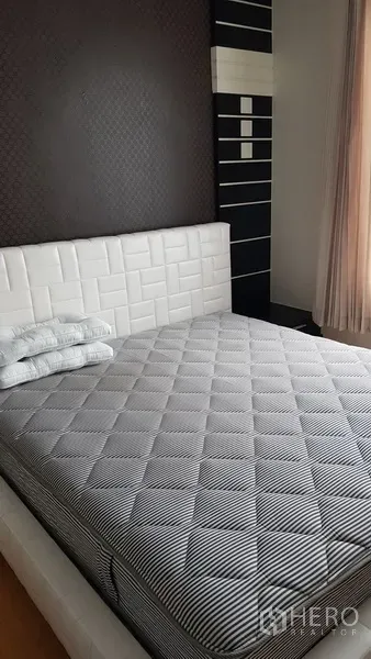 Condominium for rent in Ratchathewi, Bangkok - Bright bedroom with white upholstered headboard, striped mattress and a dark accent wall by the window.
