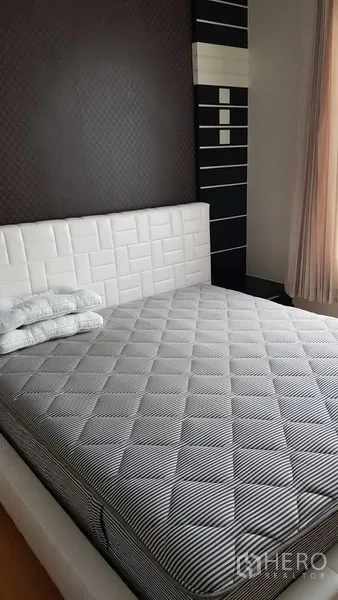 Condominium for rent in Ratchathewi, Bangkok - Bright bedroom with white upholstered headboard, striped mattress and a dark accent wall by the window.
