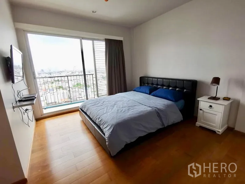 คอนโด ให้เช่าในKhlong San, Bangkok - ห้องนอนใหญ่เตียงคู่ โต๊ะข้างเตียง และประตูกระจกสไลด์ออกสู่ระเบียงวิวเมือง