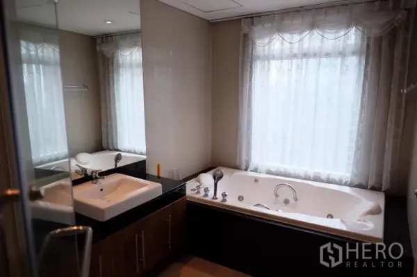 Condominium for rent in Watthana, Bangkok - Bathroom featuring a jacuzzi soaking tub, large window with sheer curtains and a sleek vanity.