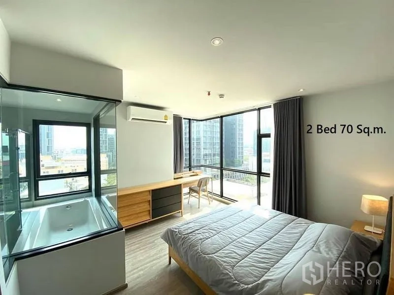 Condominium for rent in Watthana, Bangkok - Corner master bedroom with panoramic windows, built-in desk and glass-enclosed bathtub.