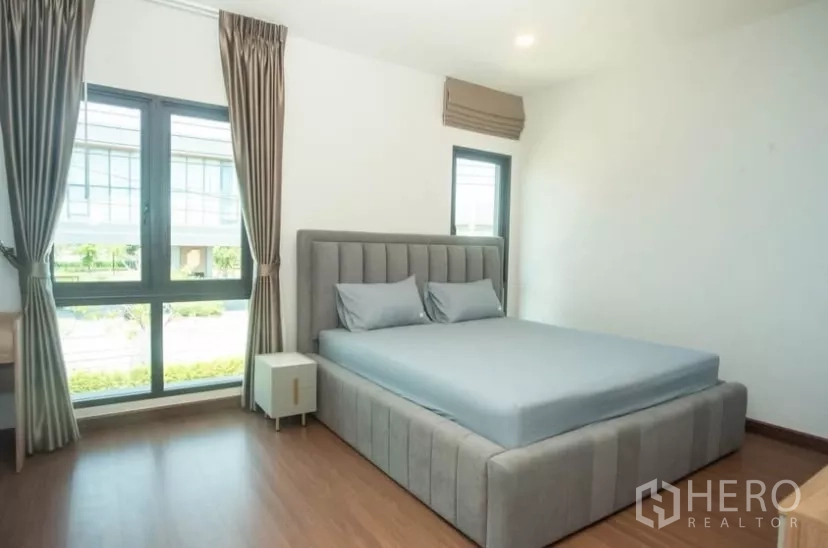 Detached House for rent in Bang Phli, Samut Prakan - Third bedroom with gray padded bed, large windows and floor-length drapes.