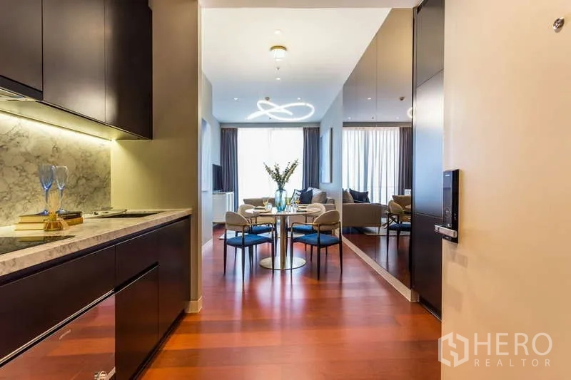 公寓 出租在Watthana, Bangkok - 入口走廊带长形厨房与镜面墙，通向明亮的用餐区和客厅。