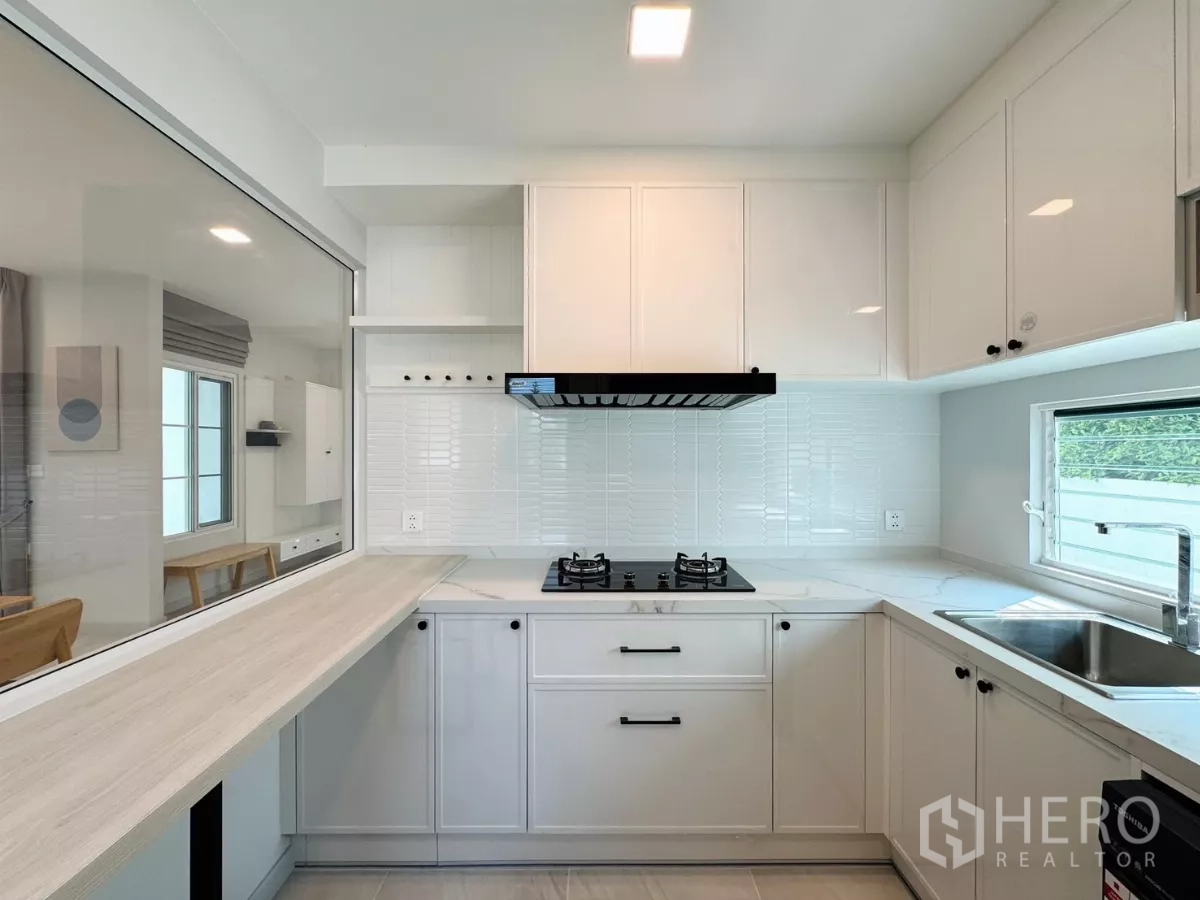 Detached House for rent in Bang Phli, Samut Prakan - Compact white kitchen with gas hob, range hood and a serving counter.