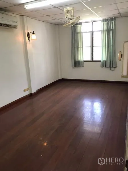 Townhouse for rent in Khlong Toei, Bangkok - Spacious room with wood floors, window drapes, AC and ceiling fan.