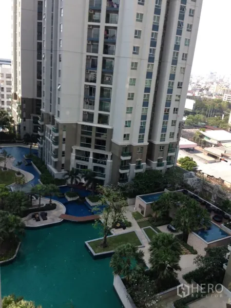 Condominium for rent in Huai Khwang, Bangkok - High-rise condominium exterior overlooking a large pool deck, greenery and distant city skyline.