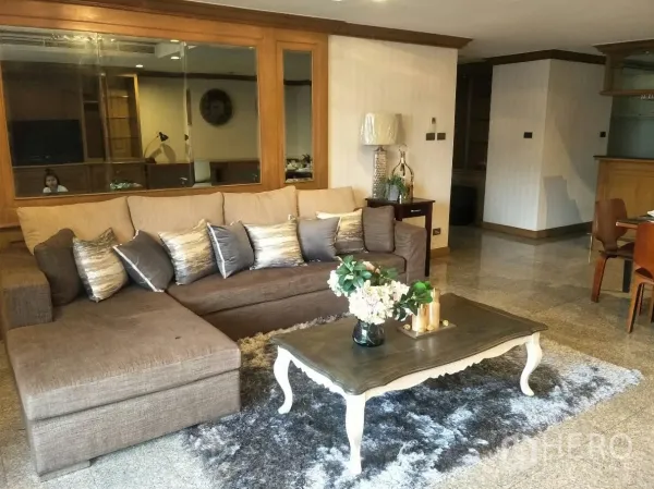 คอนโด ให้เช่าในWatthana, Bangkok - ห้องนั่งเล่นอบอุ่น โซฟา L‑shape พรมและโต๊ะกลาง ข้างผนังกระจกเงา