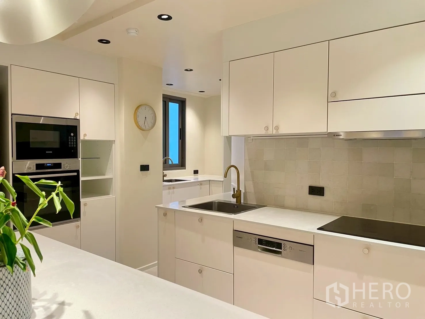 Condominium for sale in Watthana, Bangkok - Sleek white kitchen with electric cooktop, dishwasher, and gold faucet.