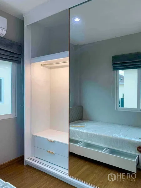 独立式住宅 出租在Bang Khen, Bangkok - 带灯开放区的镜面移门衣柜，旁边是带抽屉的床。