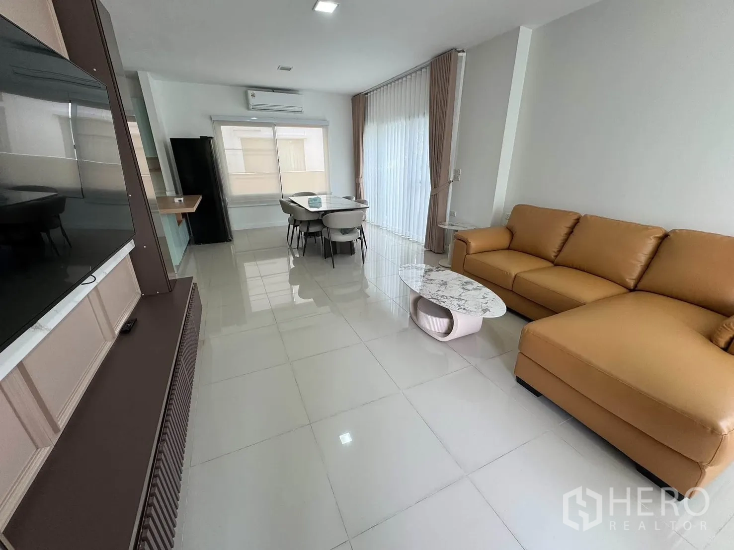 บ้านเดี่ยว for rent in Prawet, Bangkok - มุมห้องนั่งเล่นพร้อมโซฟาหนังเข้ามุม ผนังทีวี และพื้นกระเบื้องเงา