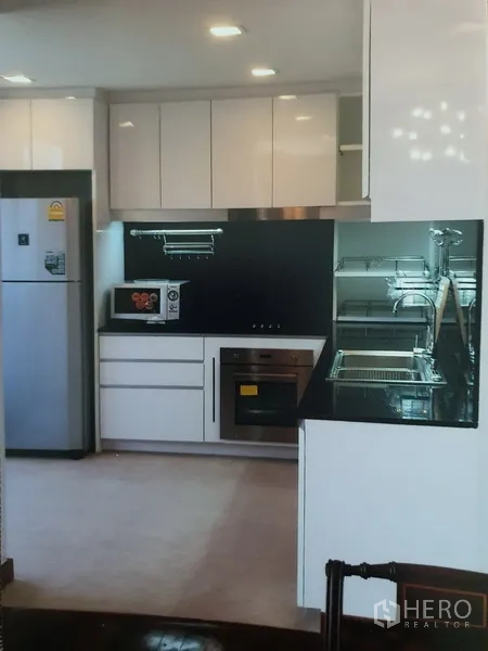 คอนโด ให้เช่าในWatthana, Bangkok - ครัวรูปตัวแอลสมัยใหม่ ตู้สีขาว ท็อปสีดำ เตาอบบิลท์อิน และไมโครเวฟ