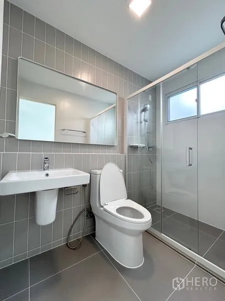 ทาวน์เฮาส์ ให้เช่า - ห้องน้ำสไตล์โมเดิร์น พร้อมฉากกั้นอาบน้ำกระจก กระจกบานใหญ่ และกระเบื้องสีเทา.